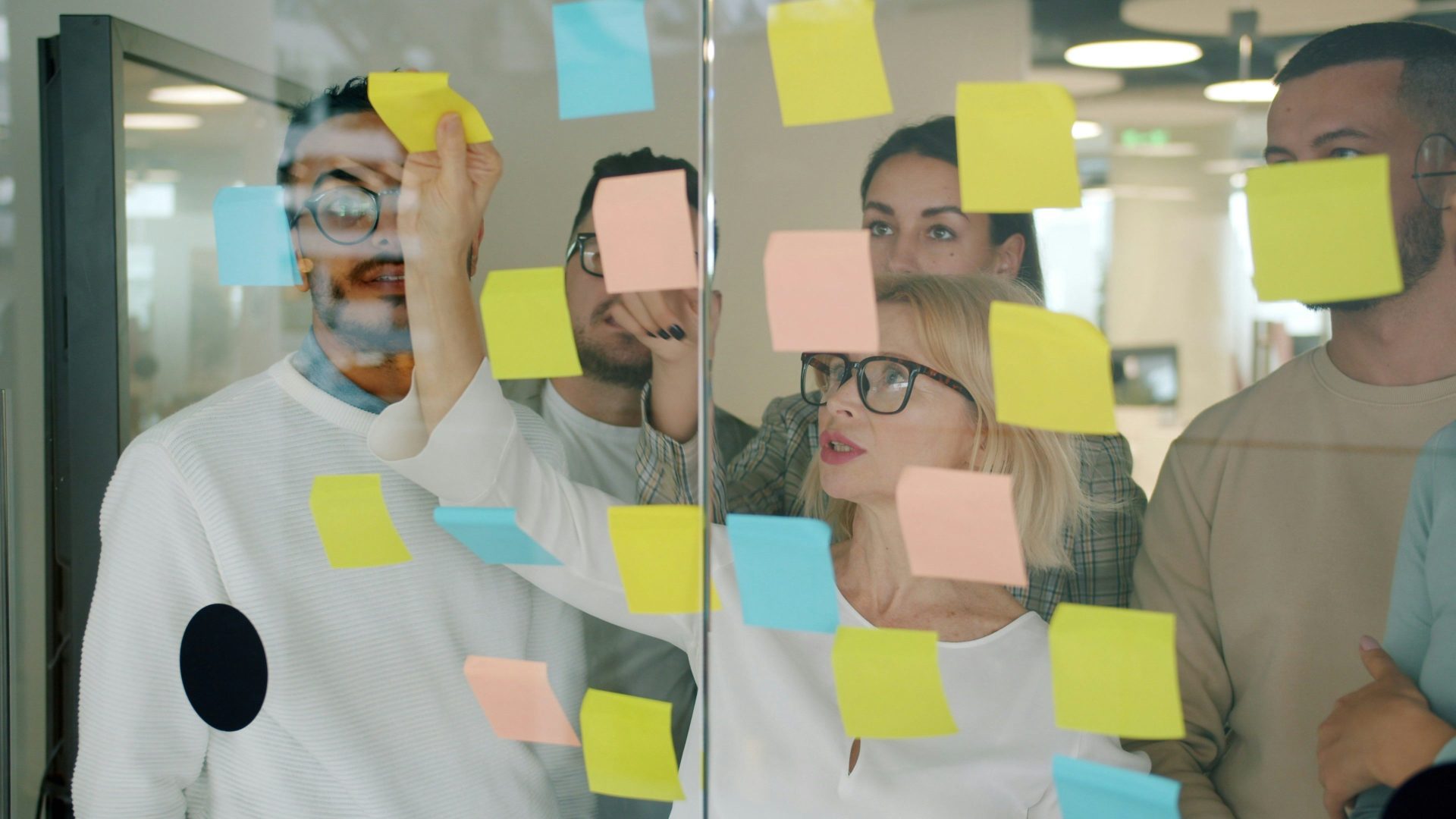 Team brainstorming with sticky notes on glass wall.